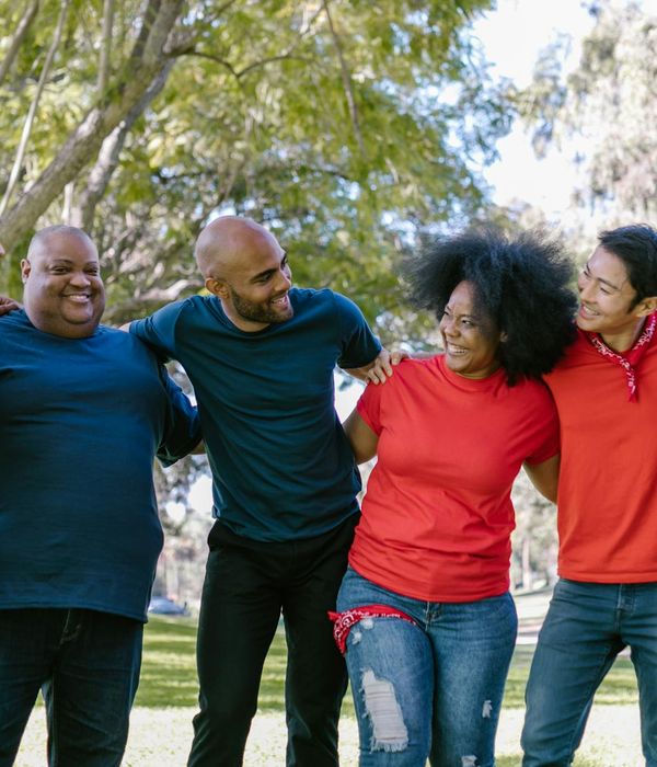 A group of diverse people smiling and stretching outdoors in a park.
